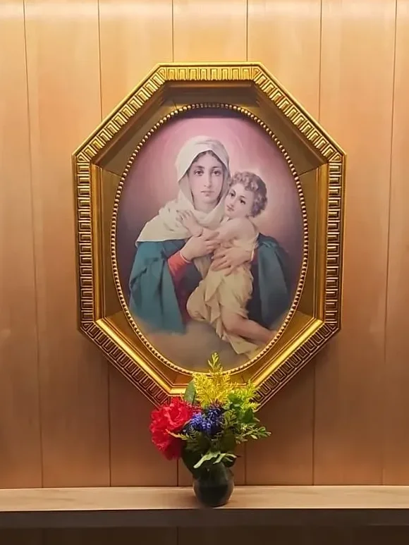 La imagen de la Mater entronizada en la Catedral de Bariloche, en su marco dorado sobre la madera, con flores