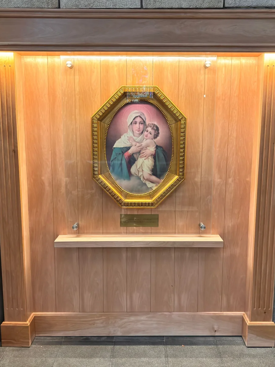La imagen de la Mater entronizada en la Catedral de Bariloche: el cuadro dorado detrás de un vidrio protector, sobre un retablo de madera iluminado
